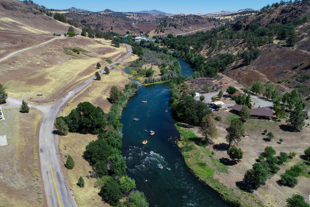 Rafters float the Klamath River, with Iron Gate Dam looming in the distance.
